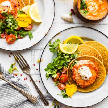 Two plates with servings of chickpea pancakes topped with harissa yogurt sauce.