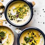 Three bowls filled with creamy cauliflower soup topped with fresh herbs and peppercorns.