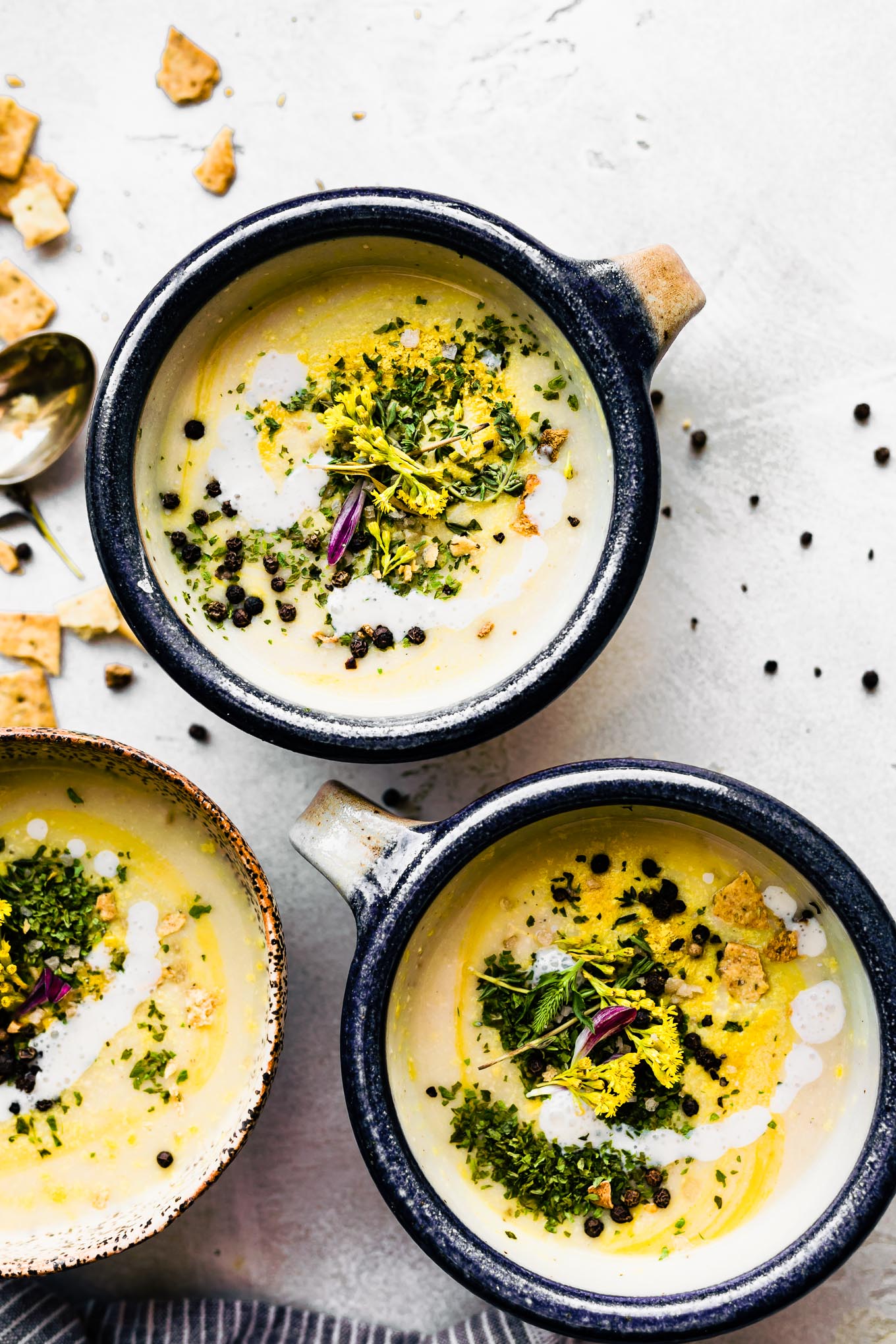 vegan cauliflower soup with fennel served in small bowl, topped with fresh herbs and peppercorns.