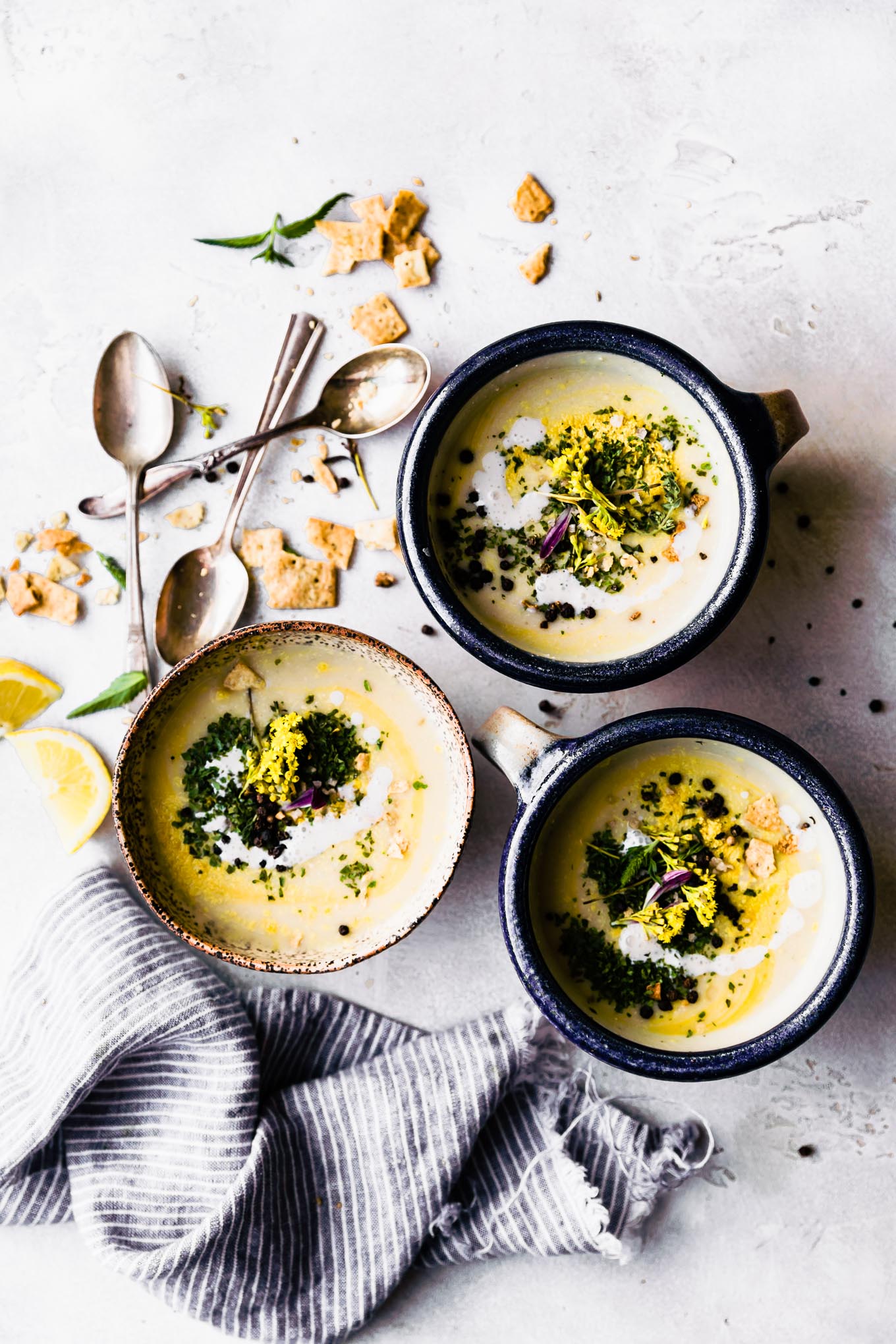 3 bowls of vegan creamy roasted cauliflower soup topped with fresh herbs and peppercorns.