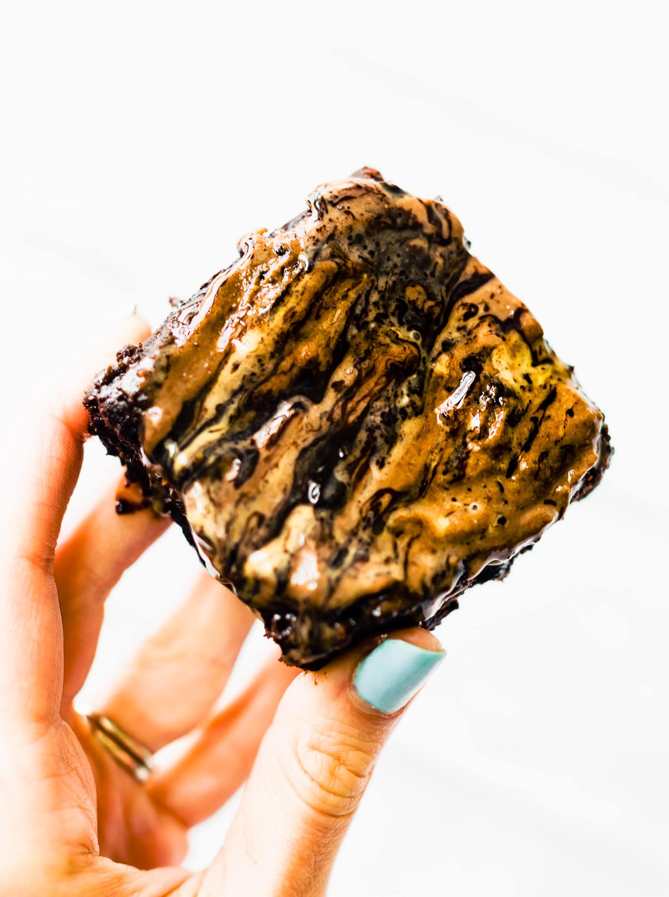 A single square maple tahini brownie with tahini frosting swirled on top being held against white background.