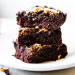 Three square pieces low carb brownies with maple tahini topping stacked up on each other.