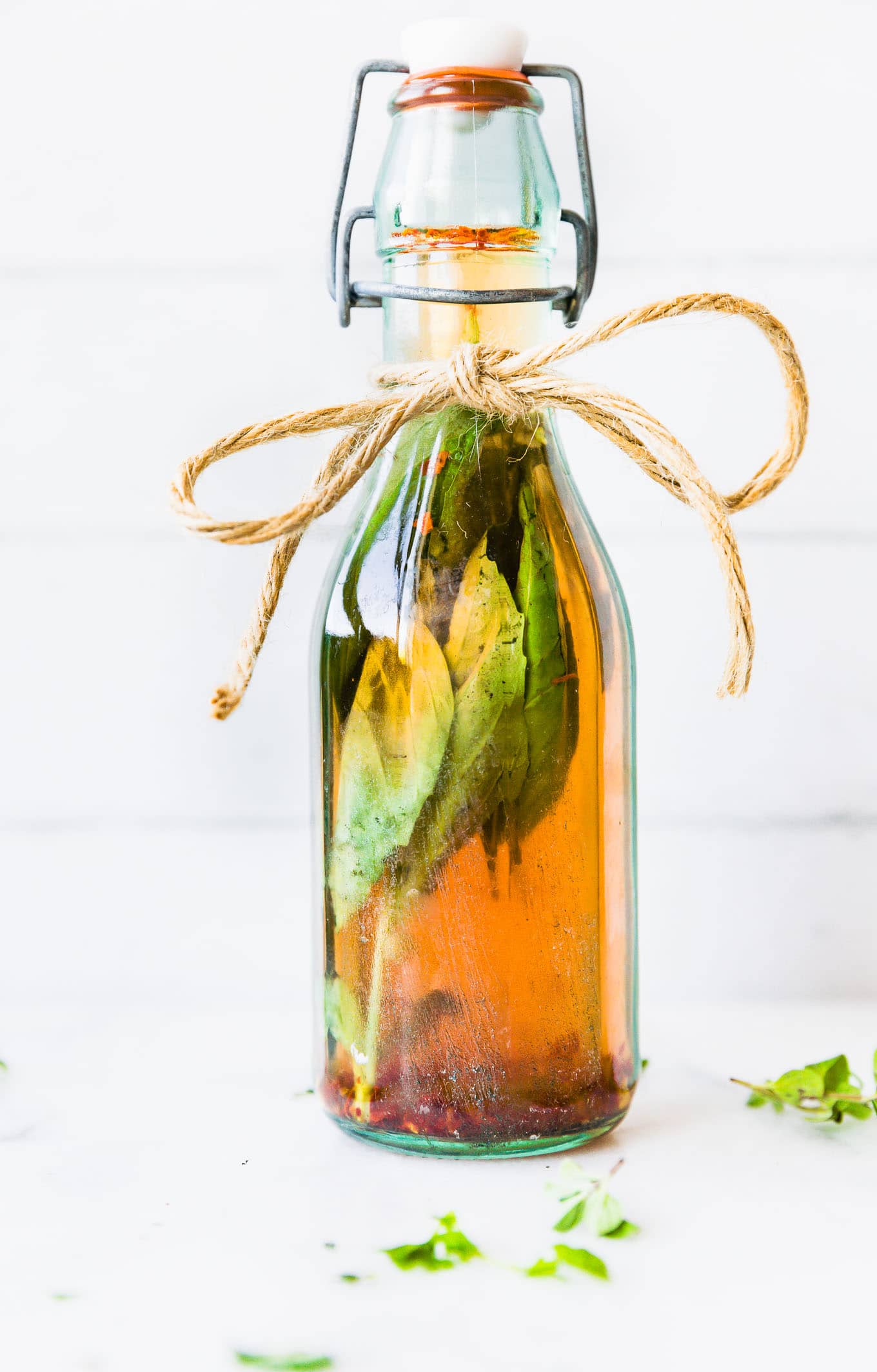 A glass bottle of vinegar with fresh herbs in it, twine tied in a bowl around top of jar.
