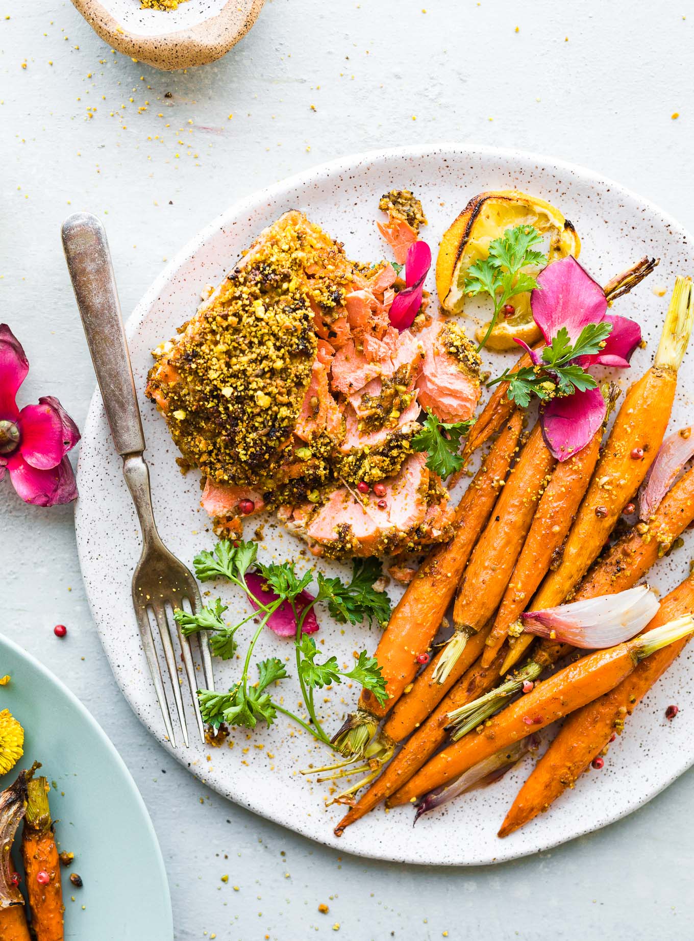 White and brown speckled plate with serving of pistachio crusted salmon fillet, glazed carrots on the side.