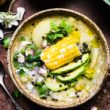 Bowl of chicken potato soup with corn on the cob, avocado, cilantro, and pepper