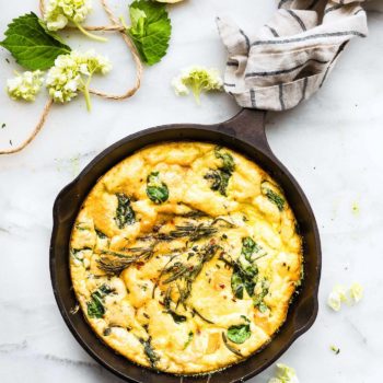 Overhead view cast iron skillet with pumpkin frittata topped with herbs.