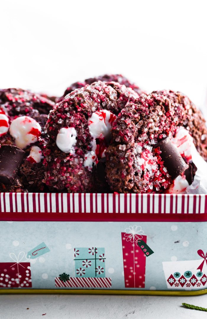 Close up side view of peppermint chocolate cookies coated in red and white sugar in a striped Christmas cookie tin.
