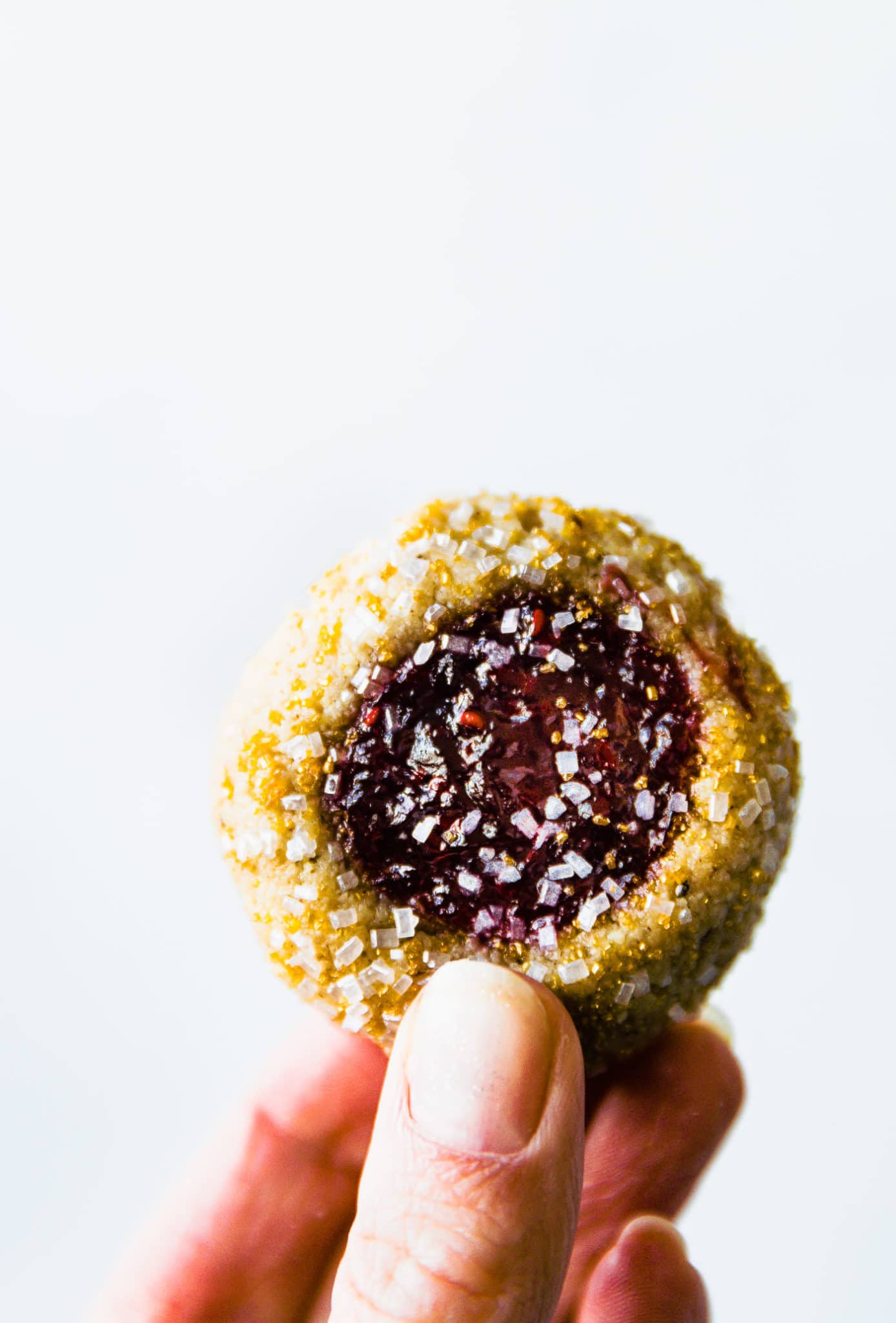 A hand holding a vegan raspberry thumbprint cookie topped with sparkling sugar