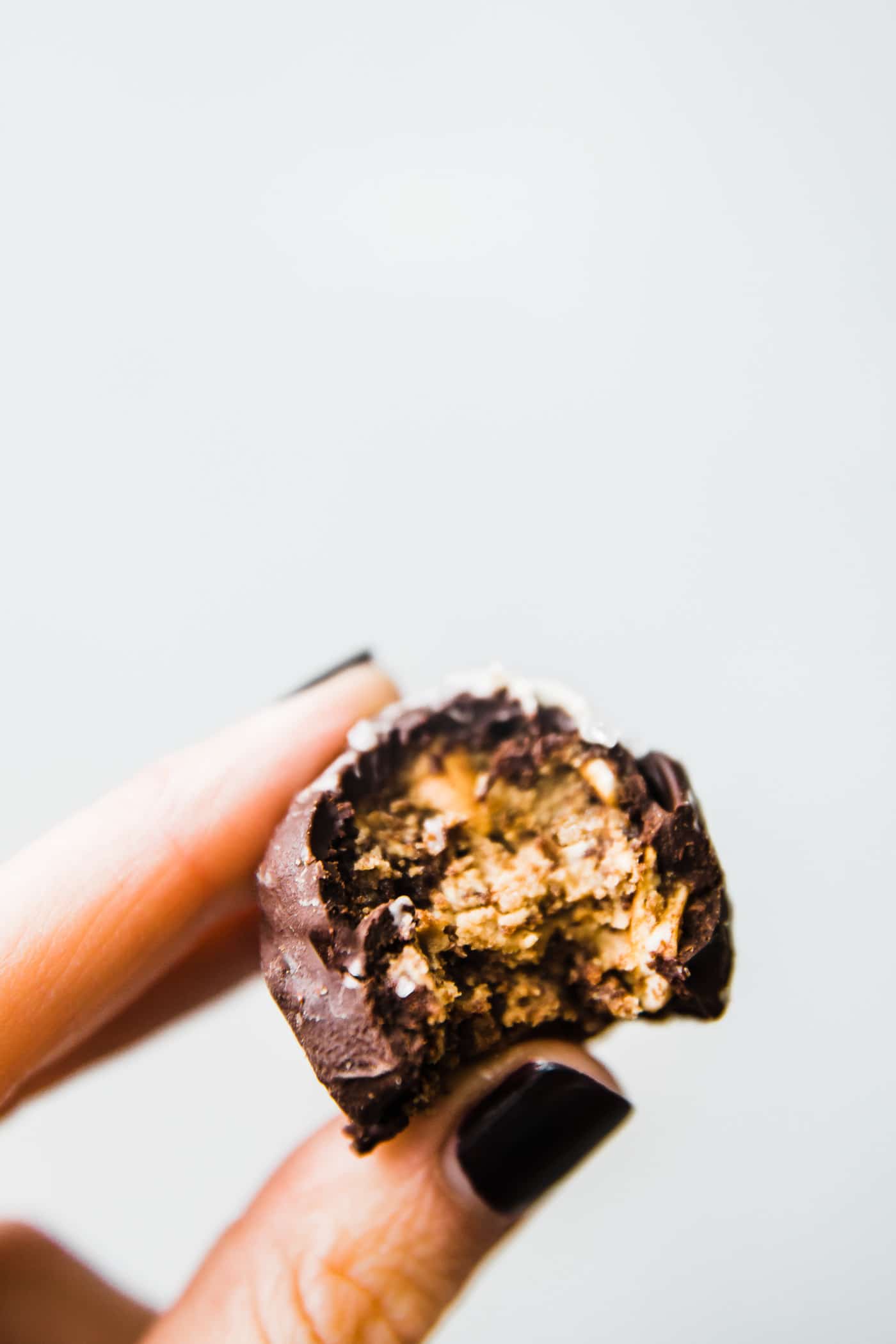A cookie truffle coated in chocolate with bite taken out to show inside texture being held between thumb and forefinger.