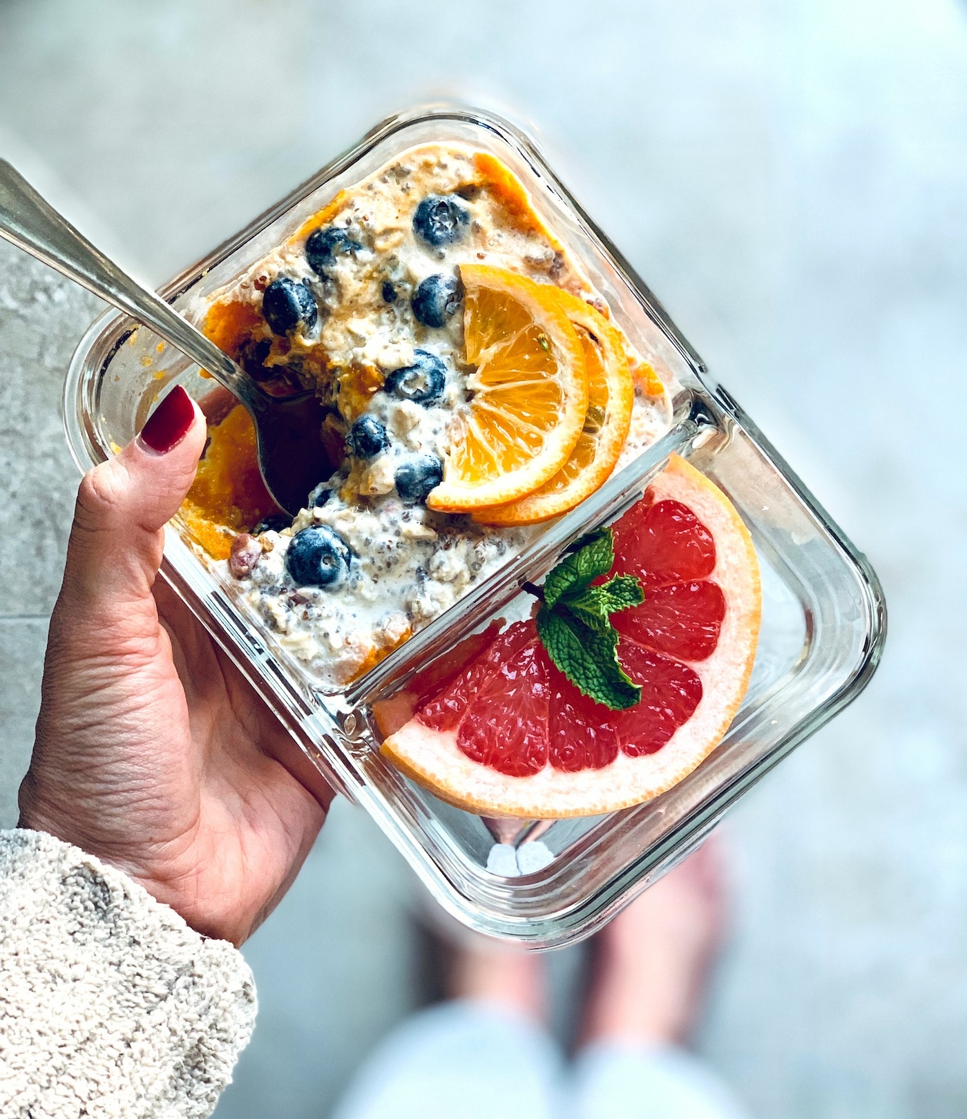 A woman's hand holding glass meal prep container filled with overnight oatmeal and fresh fruit.
