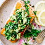 Overhead view pan seared salmon fillet topped with avocado gremolata on brown speckled plate.