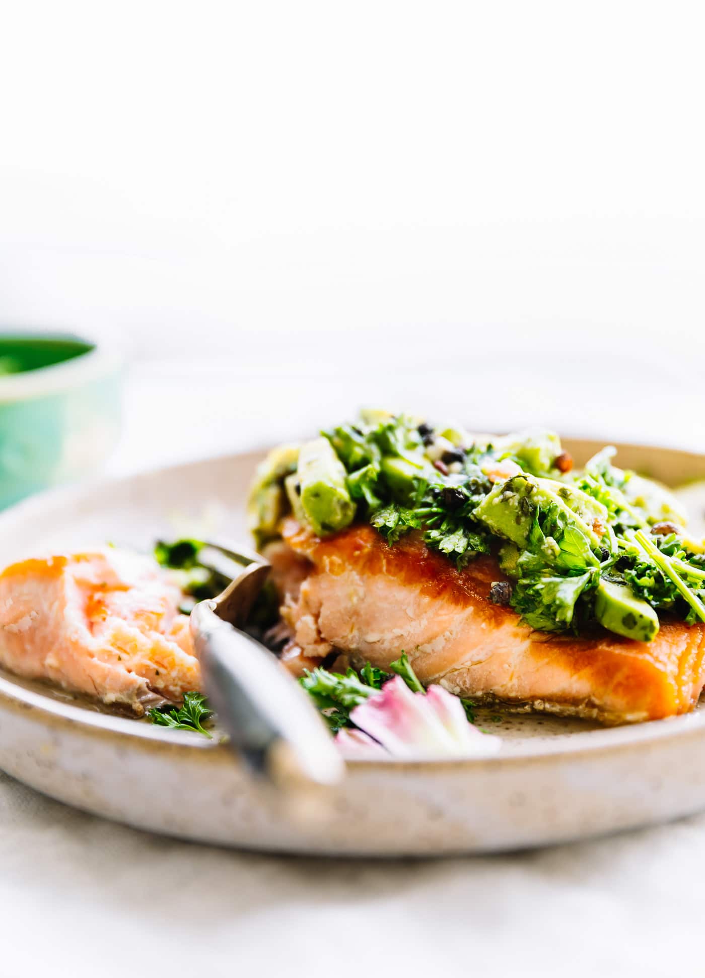 A fork cutting into a pan seared salmon fillet topped with avocado gremolata.