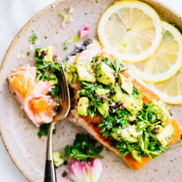 Overhead view pan seared salmon fillet topped with avocado gremolata serving on brown speckled plate.
