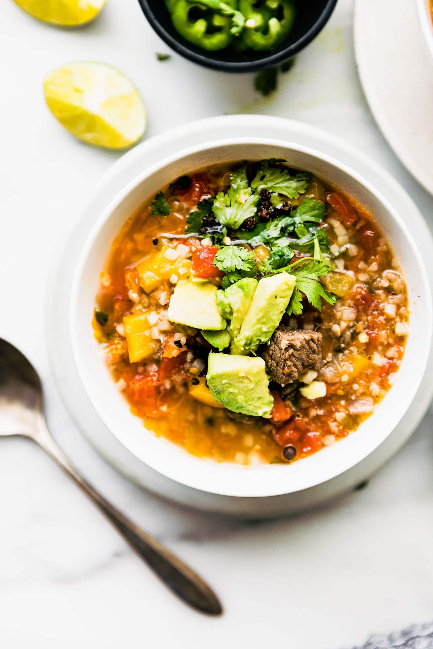 mexican instant pot steak soup in a white bowl topped with avocado pieces and fresh cilantro