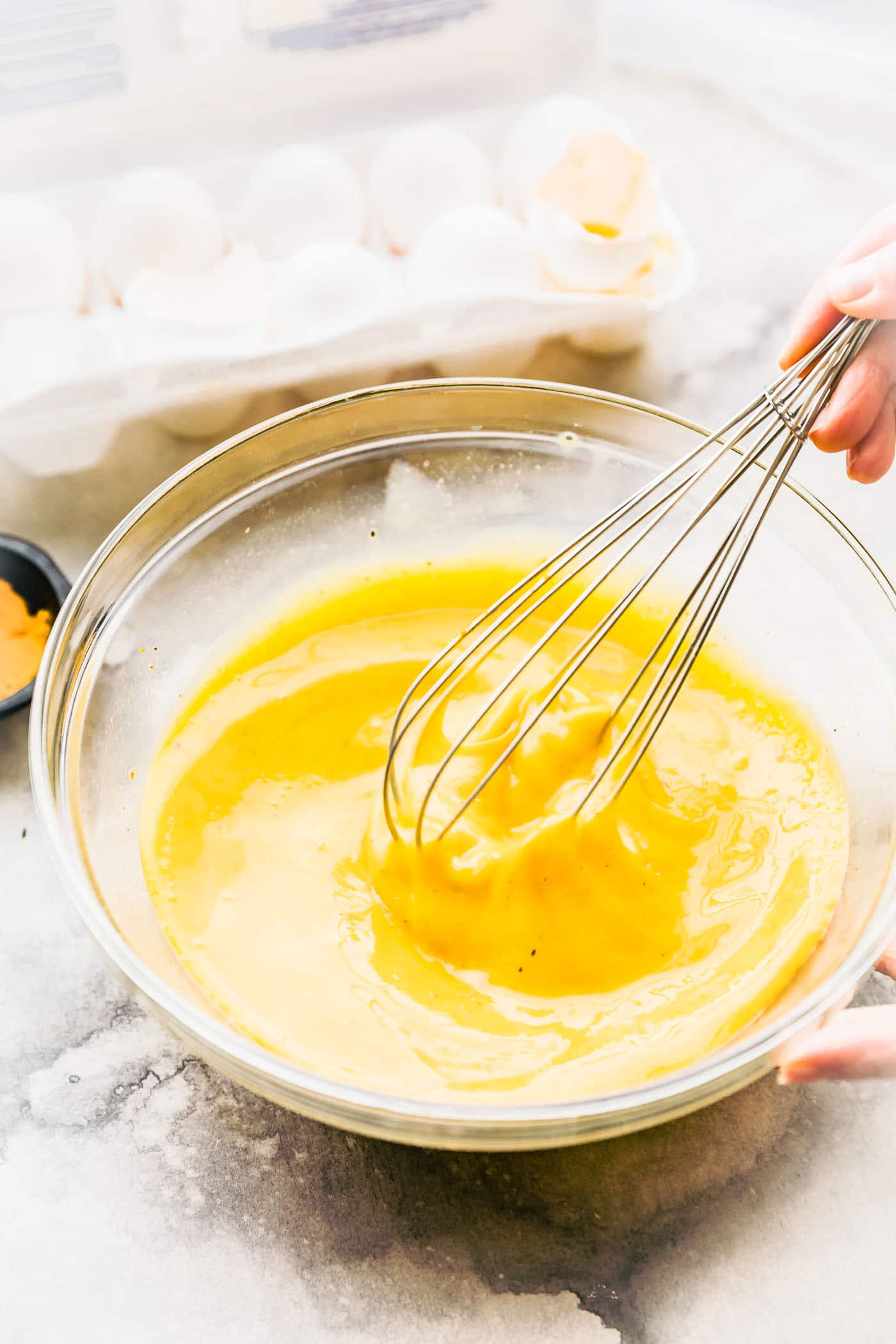 Eggs being whisked in a clear glass mixing bowl.