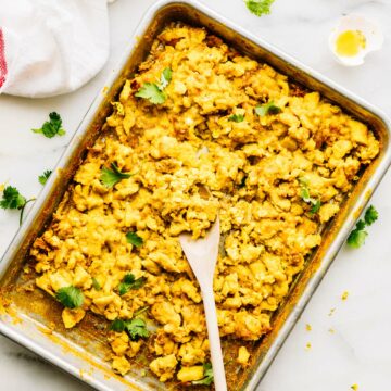sheet pan filled with turmeric scrambled eggs, a wooden spoon in the eggs.