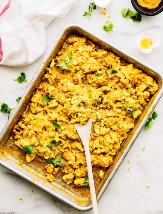 sheet pan filled with turmeric scrambled eggs, a wooden spoon in the eggs.