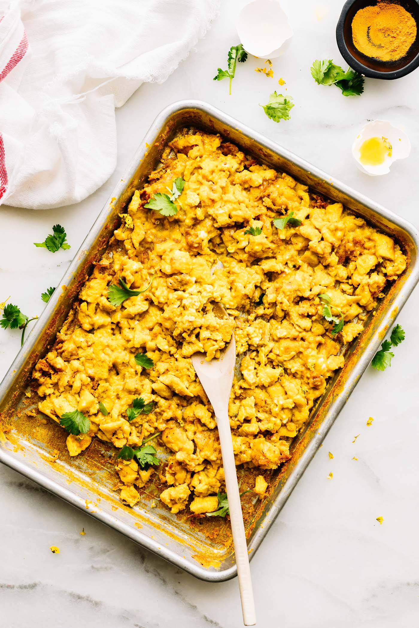 sheet pan filled with turmeric scrambled eggs, wooden spoon in eggs.