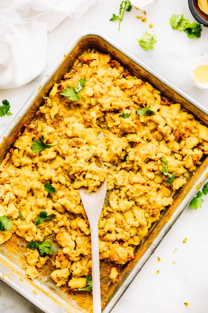 Turmeric scrambled eggs on a sheet pan with a wooden spoon in the eggs.