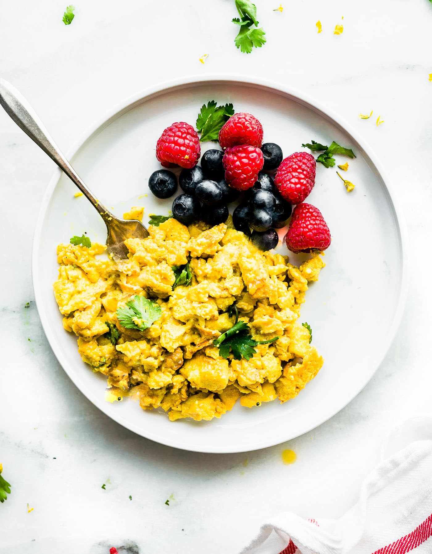 turmeric scrambled eggs on a white plate with fresh berries on the side.
