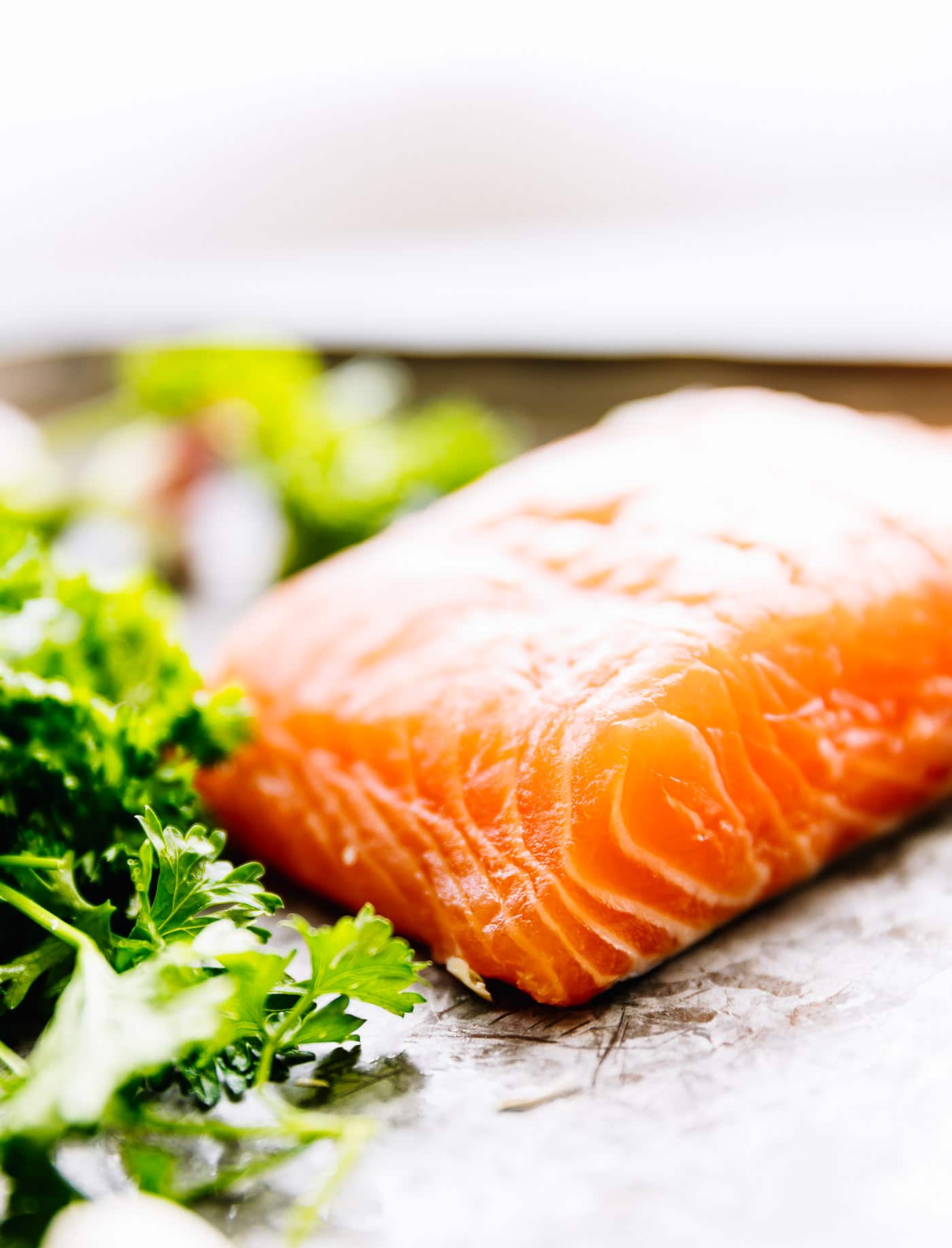 a close up image of a raw piece of salmon with greens on the side