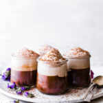 Small glass jars filled with Mexican chocolate mousse, topped with whipped cream and chocolate shavings, on a white tray.
