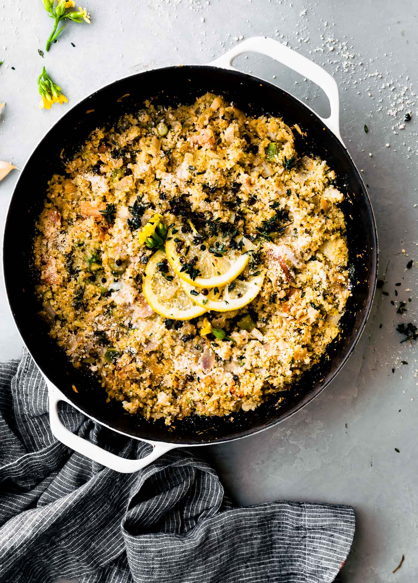 Overhead view cauliflower broccoli risotto style casserole in white and black dutch oven topped with lemon slices, thyme, and parmesan.