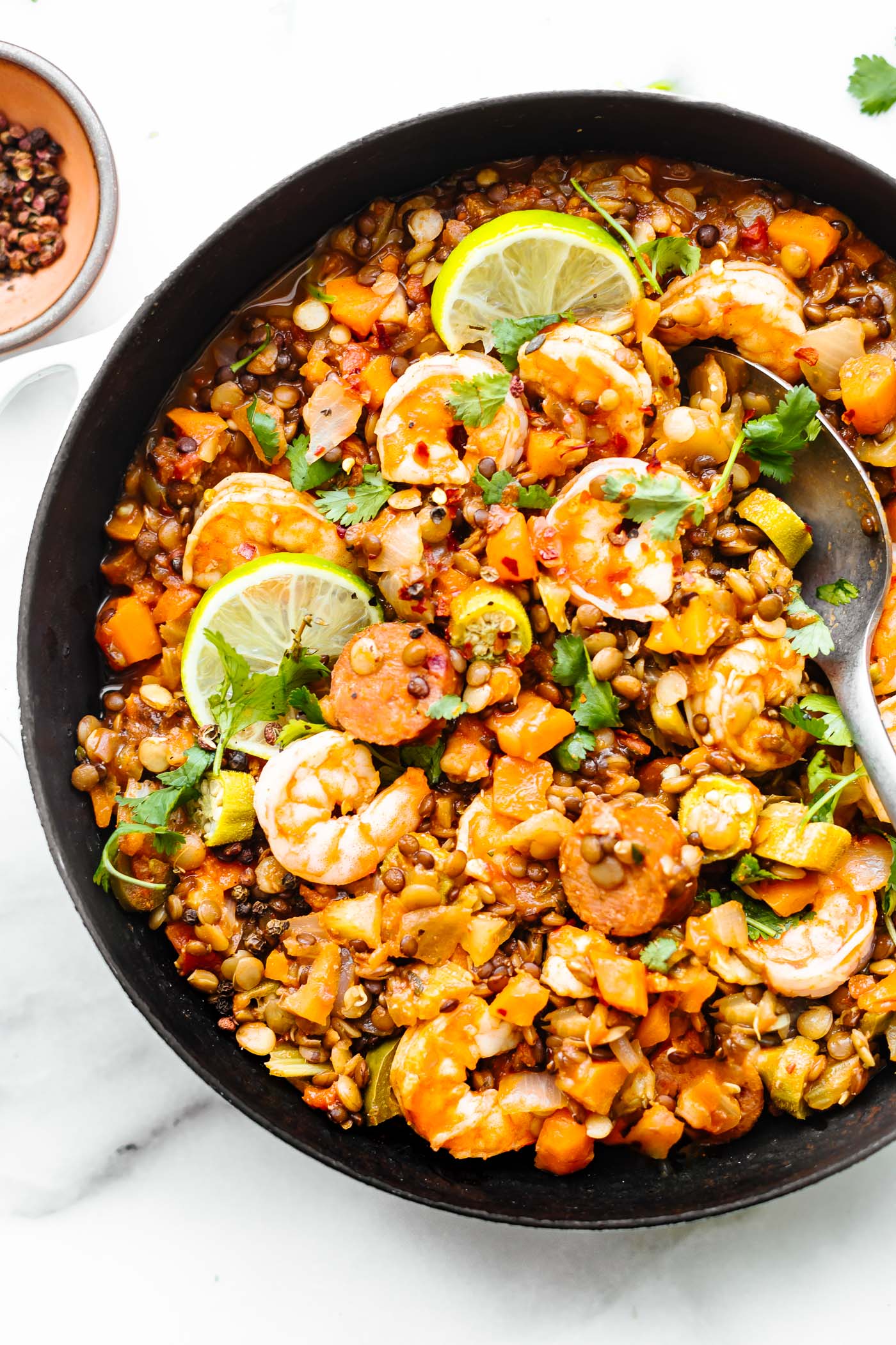 Shrimp jambalaya with lentils and sausage in a white skillet