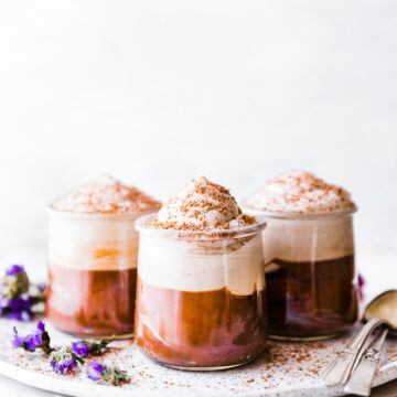 Three short glass jars filled with Mexican chocolate mousse topped with whipped cream on a white tray.
