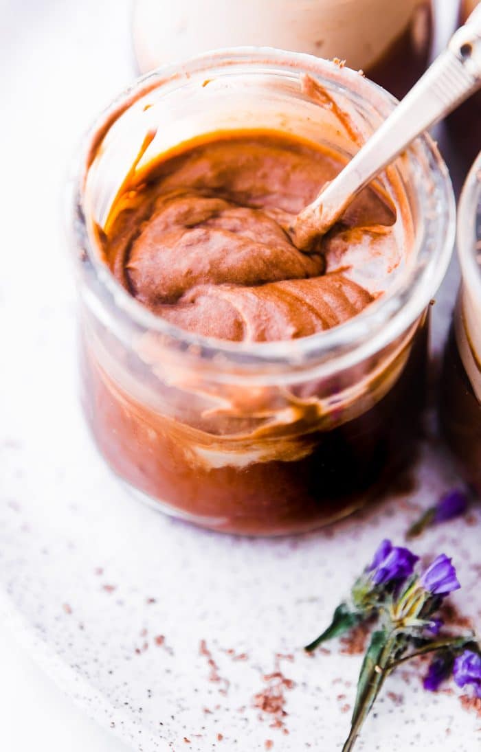 Mexican chocolate mousse in a small glass jar with a spoon stirring it together.