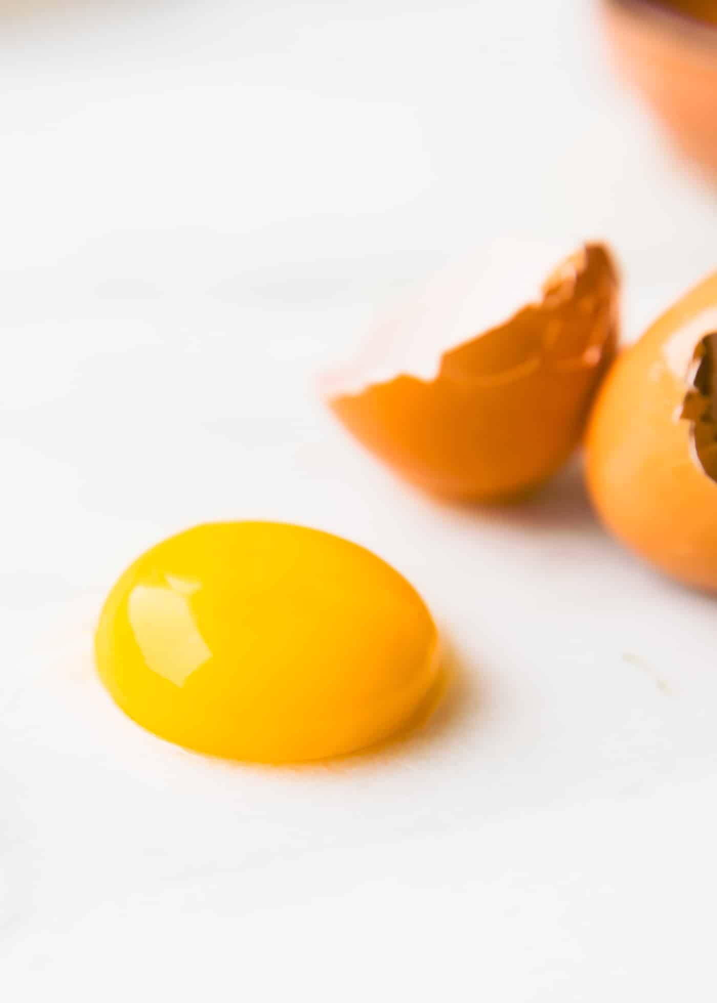 An egg yolk on counter with cracked shell in two pieces in background.