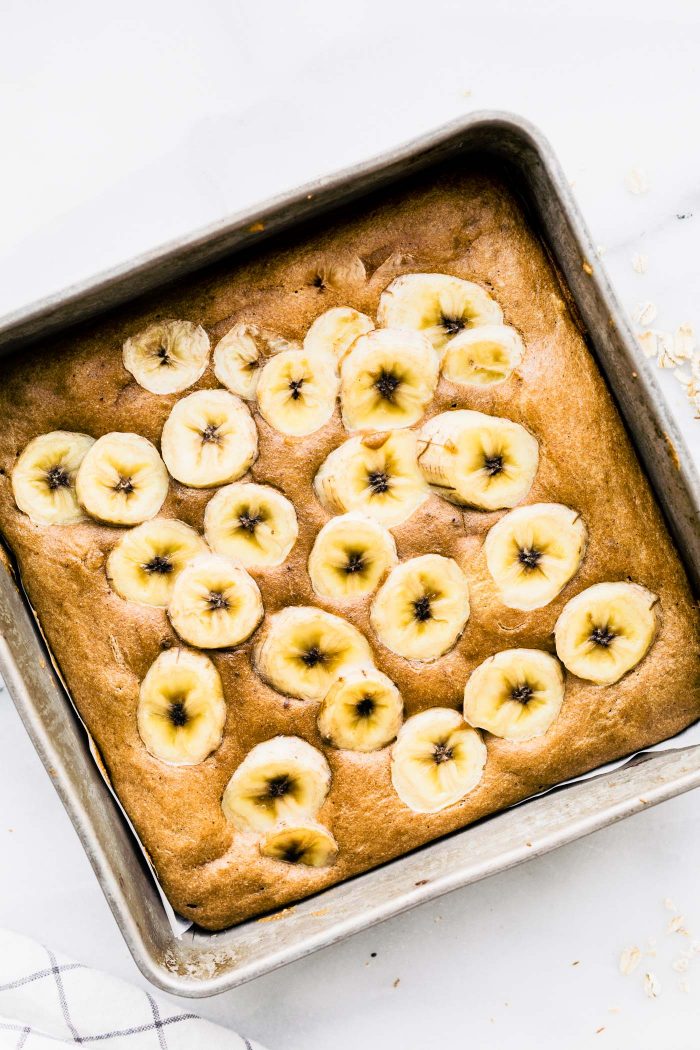 Overhead view square baking dish with flourless banana bread bars topped with banana slices.