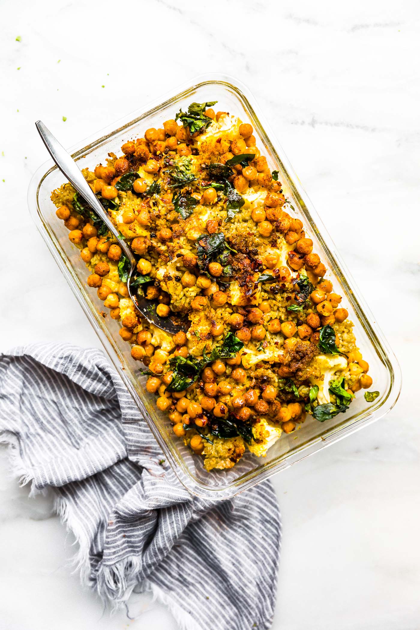 Curried Cauliflower and Chickpea Bake in clear glass baking dish with spoon in casserole.