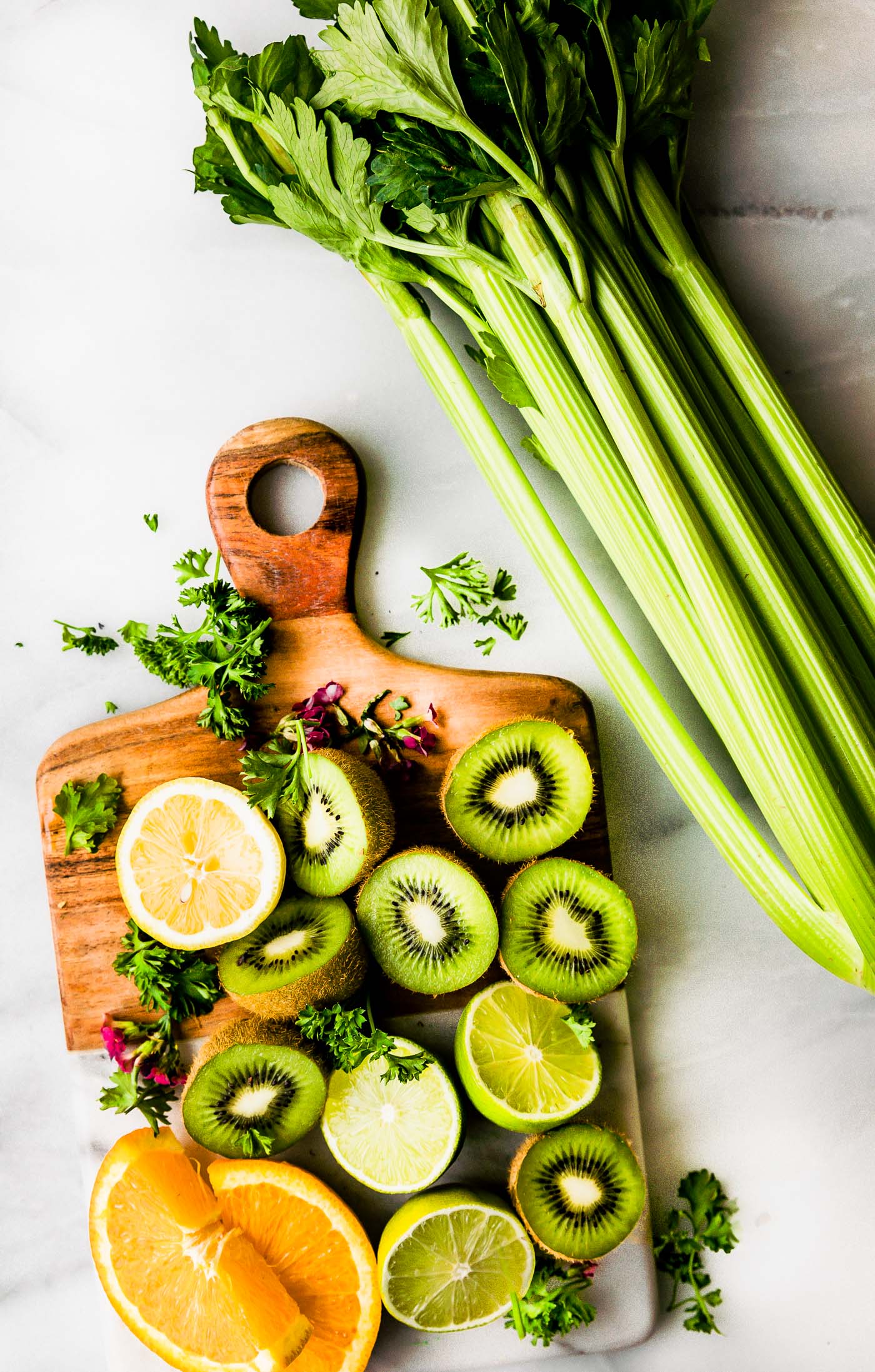 Ingredients for green smoothie arranged together on wooden cutting board.