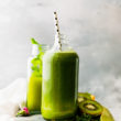 Green smoothie in a tall glass bottle on a wooden cutting board.