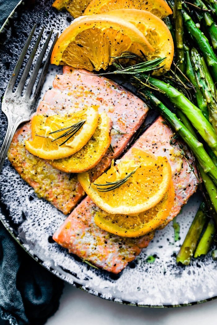 rosemary citrus baked salmon plated on grey speckled plate with side of asparagus and lemon slices.