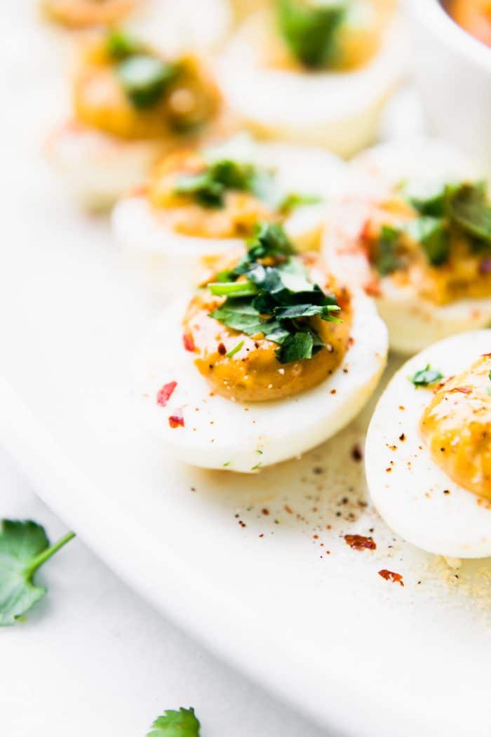 Close up view deviled eggs filled with chipotle filling and topped with fresh herbs.