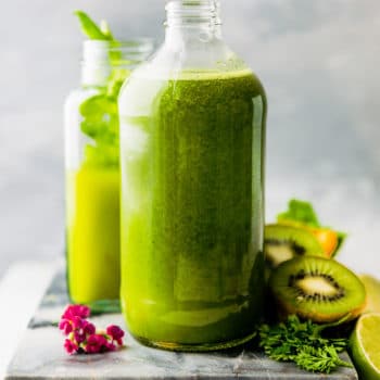 tall pitcher of detoxifying green smoothie on cutting board with fresh fruit around