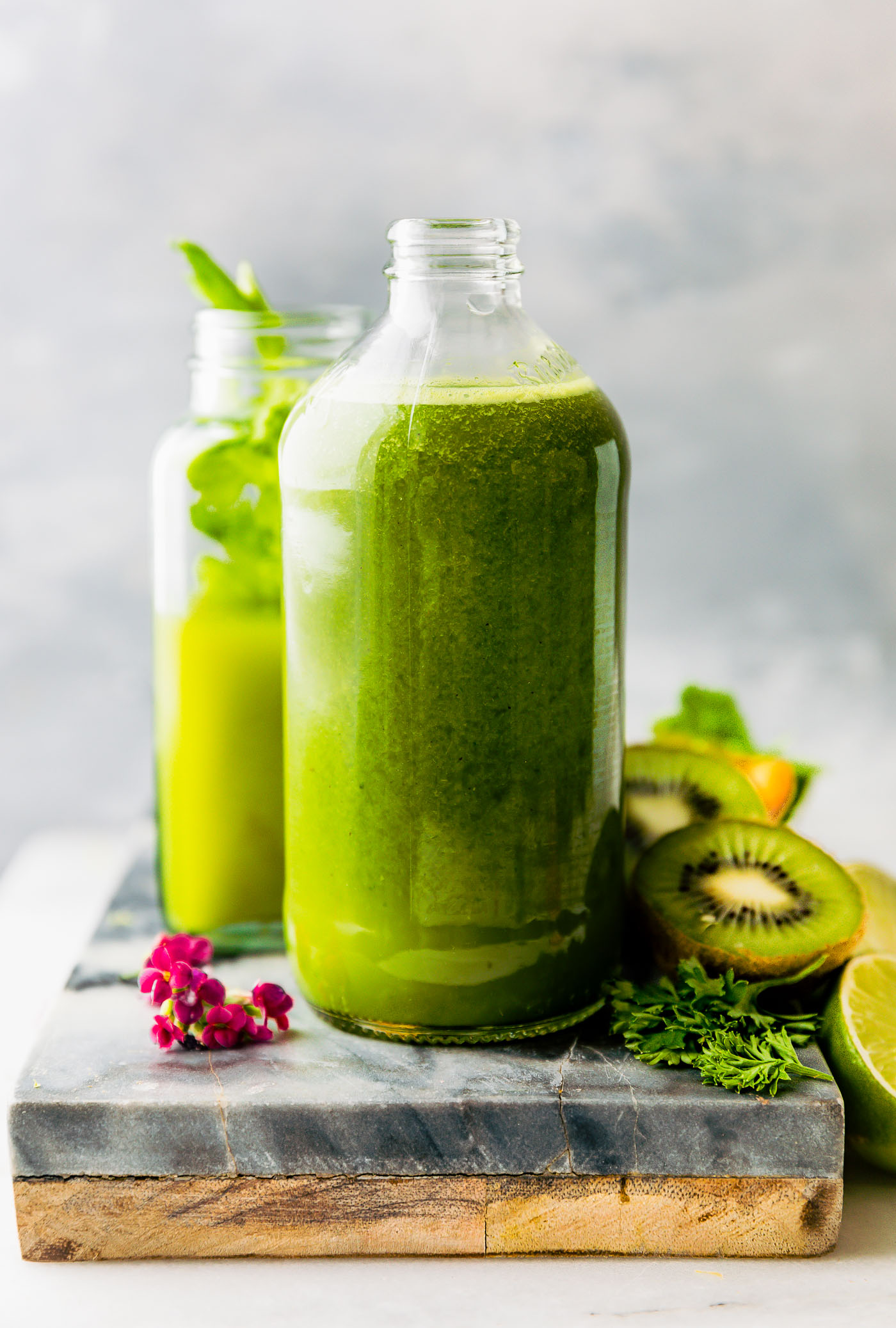 A green smoothie in tall glass bottle on wooden cutting board with cut kiwi on side.