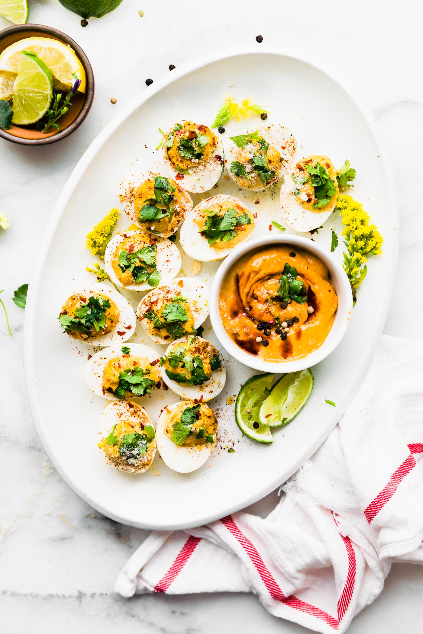 White platter of chipotle deviled eggs topped with fresh herbs, bowl of chipotle dipping sauce on side.