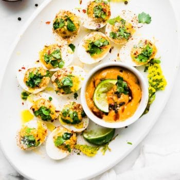 White platter filled with chipotle deviled eggs topped with fresh herbs.