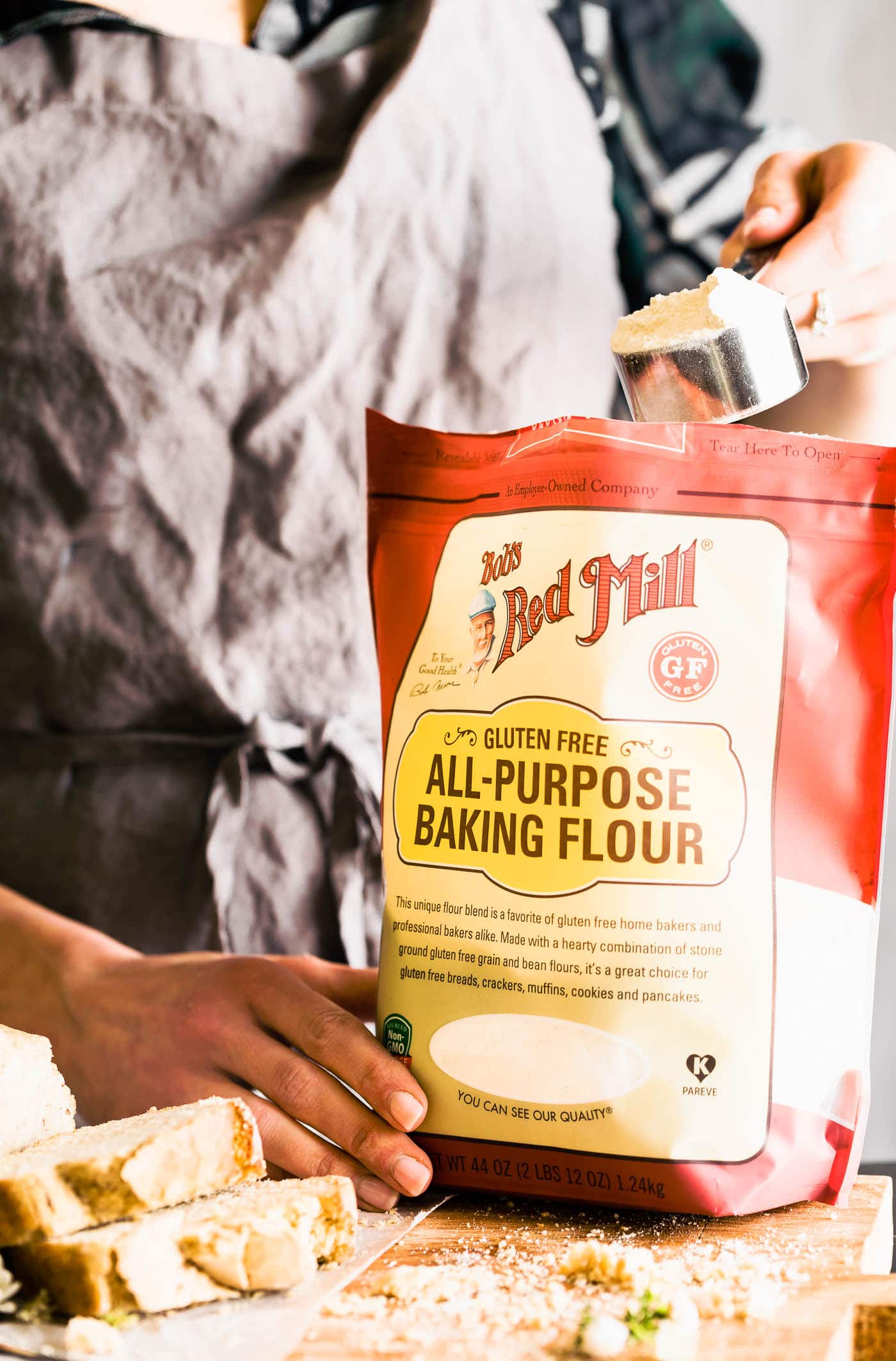 bag of bob's redmill all purpose baking flour, gluten free. woman scooping a measuring cup of flour