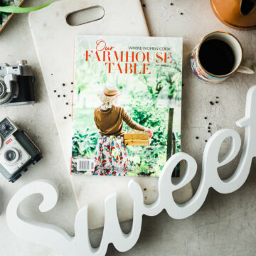 where woman cook farmhouse table magazine on table with vintage cameras and wooden word 'sweet' in white