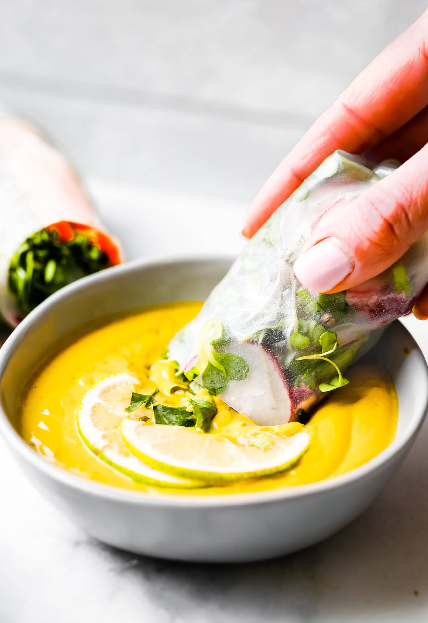 A spring roll being dipped into a bowl of ginger curry sauce.