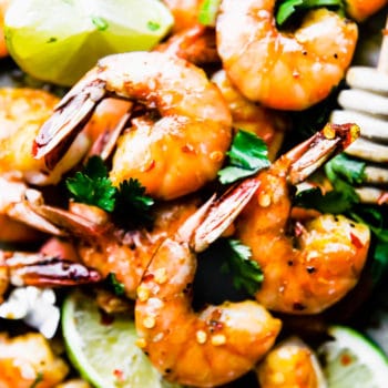 Close up view honey baked shrimp with lime slices on baking sheet.