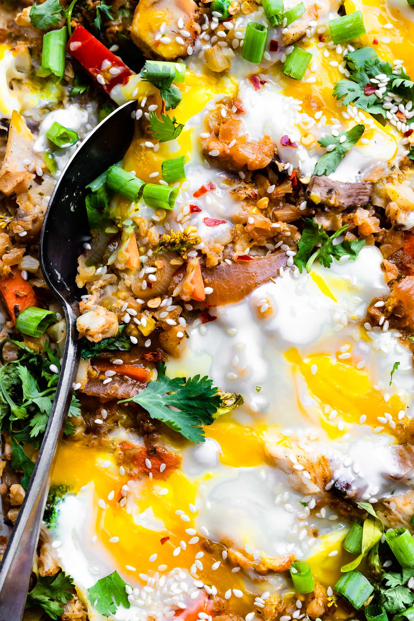 Close up view cauliflower fried rice casserole with fried eggs on top, serving spoon scooping out serving.