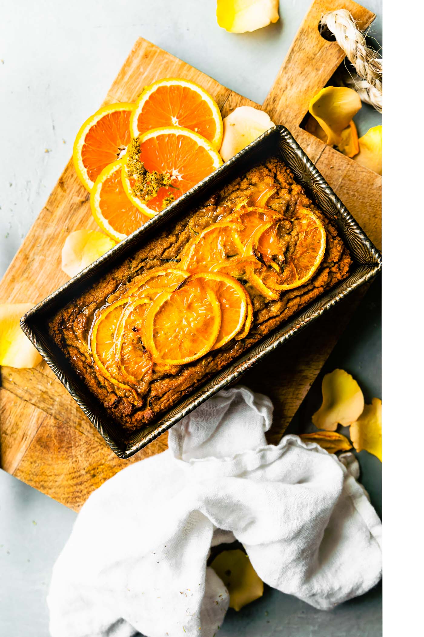 A loaf of orange zucchini bread in silver loaf pan sitting on wooden cutting board. Topped with thinly sliced orange