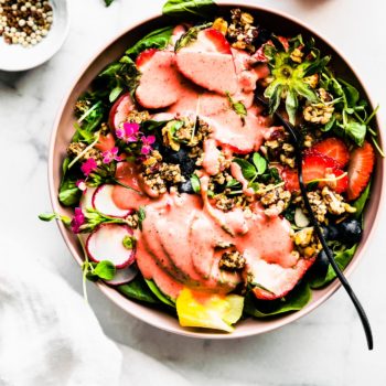 Overhead view pink bowl filled with strawberry spinach salad topped with granola croutons
