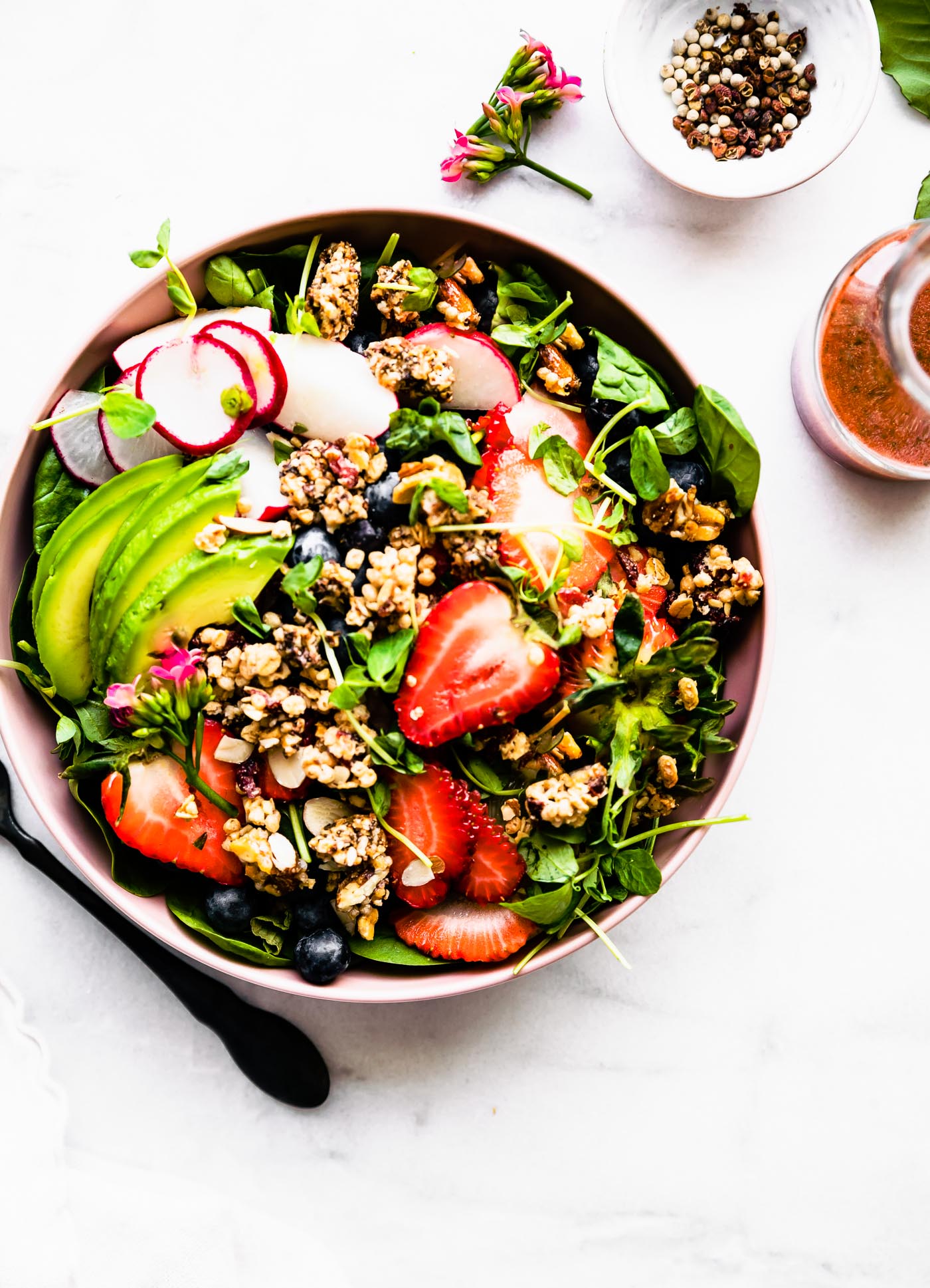 Strawberry spinach salad with vegetables and dressing served in pink bowl.