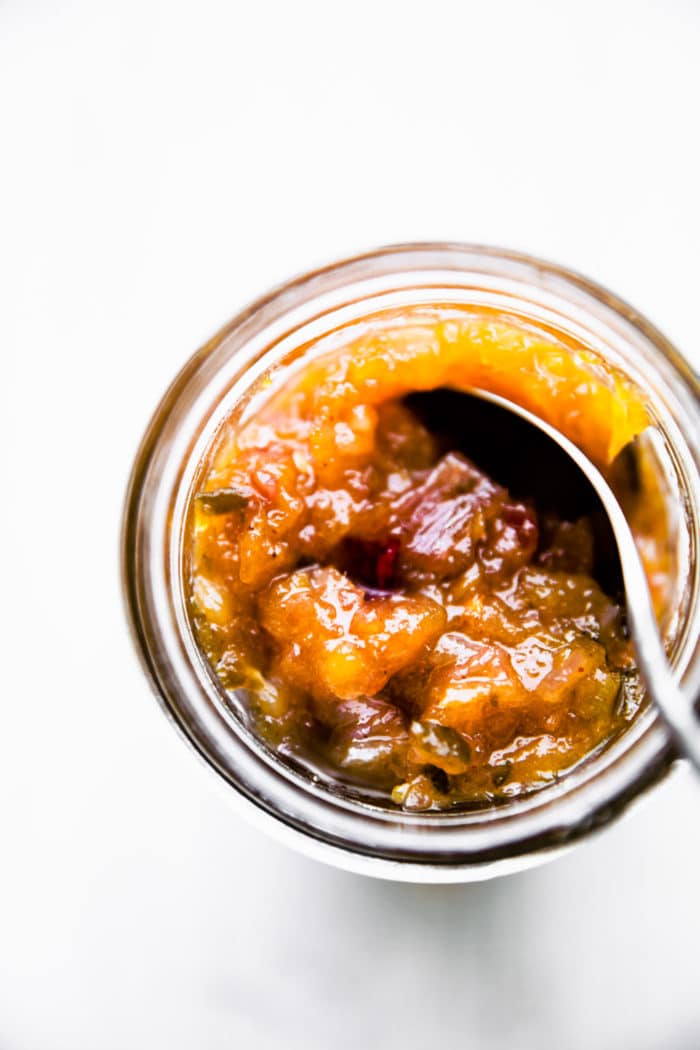 overhead view jar of spicy mango chutney with spoon scooping up serving.
